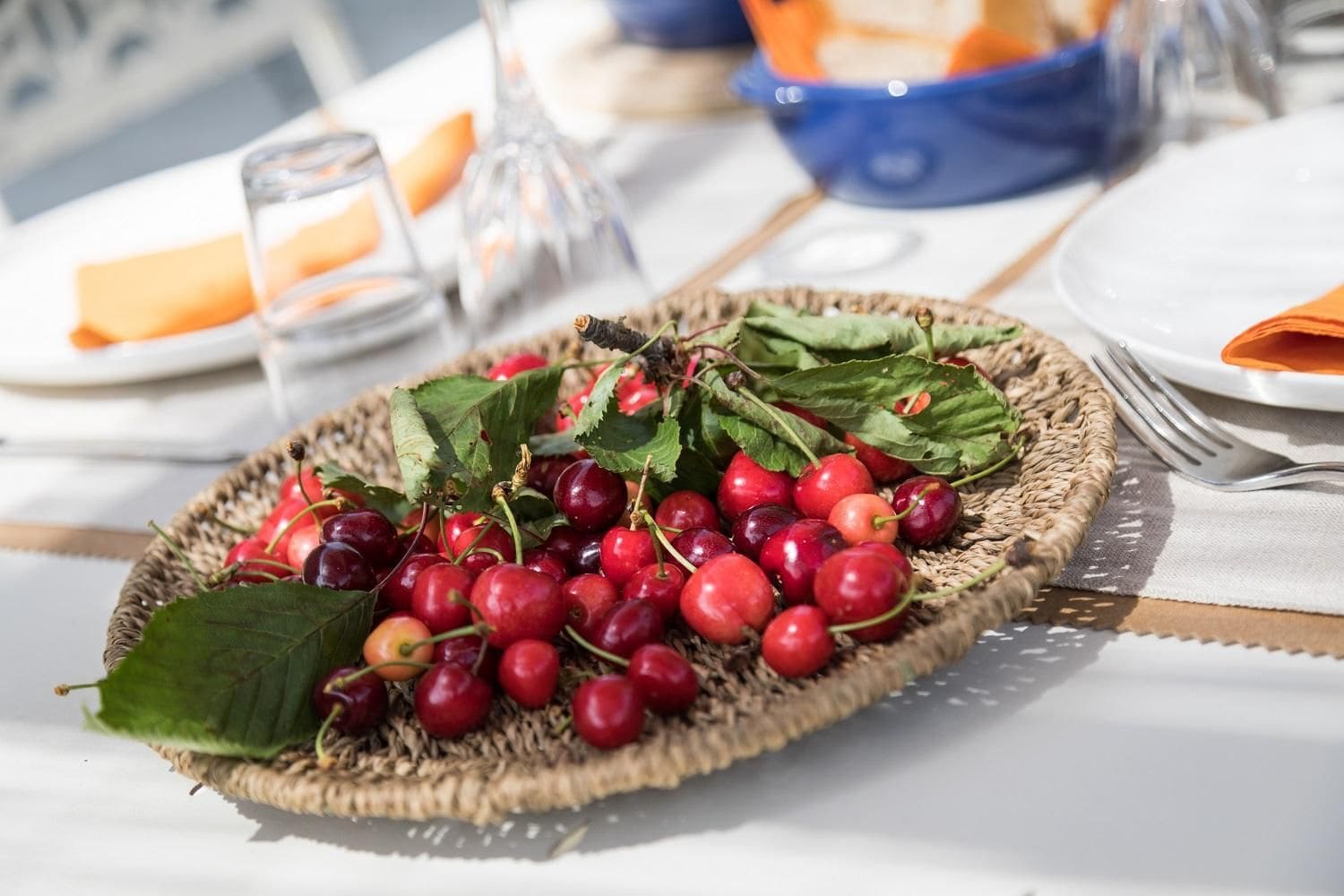 A wicker basket filled with cherries and leaves on a table.