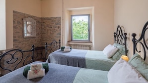 A room with two beds, stone walls, a window, and a metal headboard. - Podere Groppini (Fivizzano)