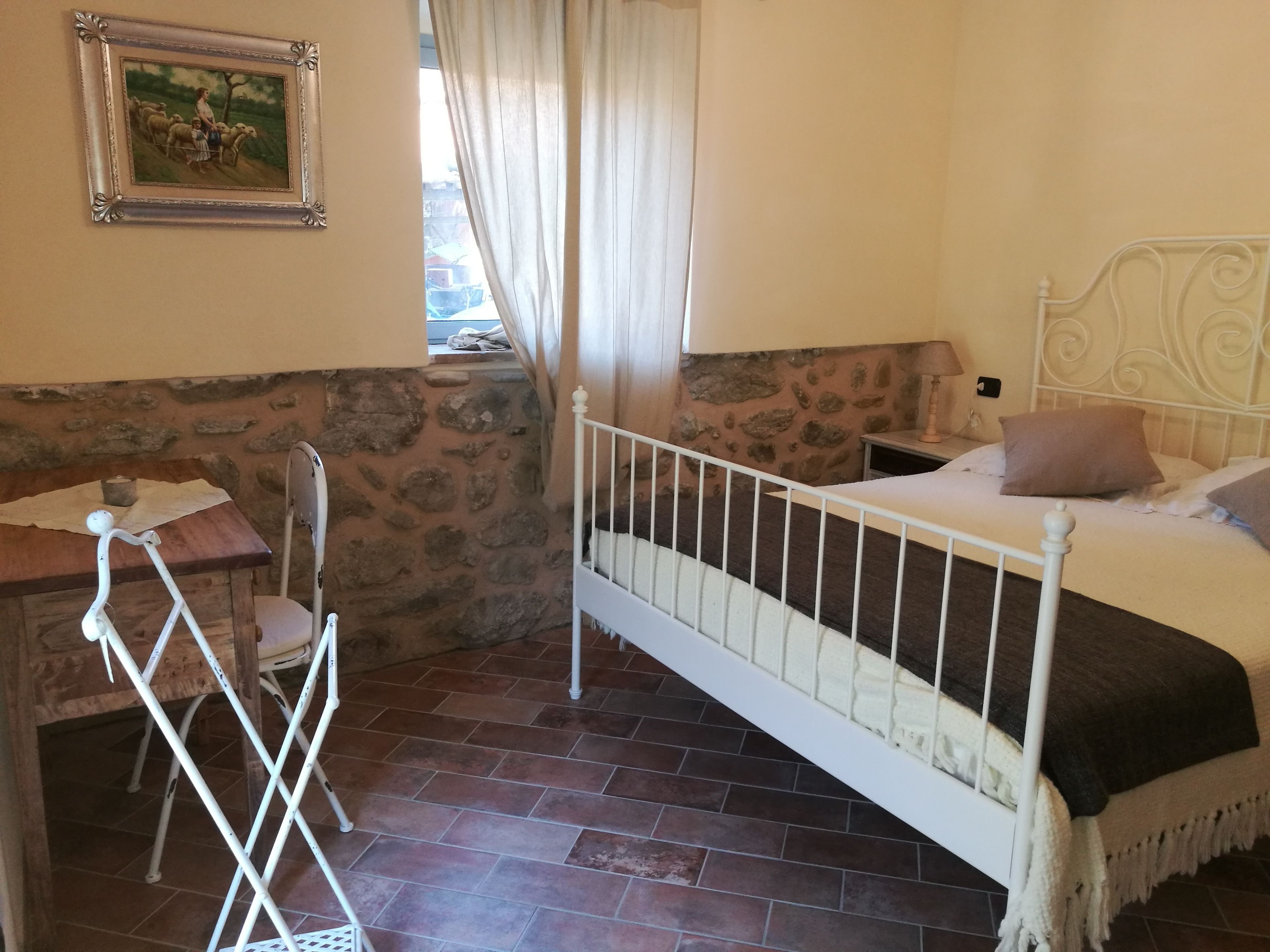 Une chambre avec un mur en pierre, un lit avec une tête de lit, un bureau en bois et une chaise.