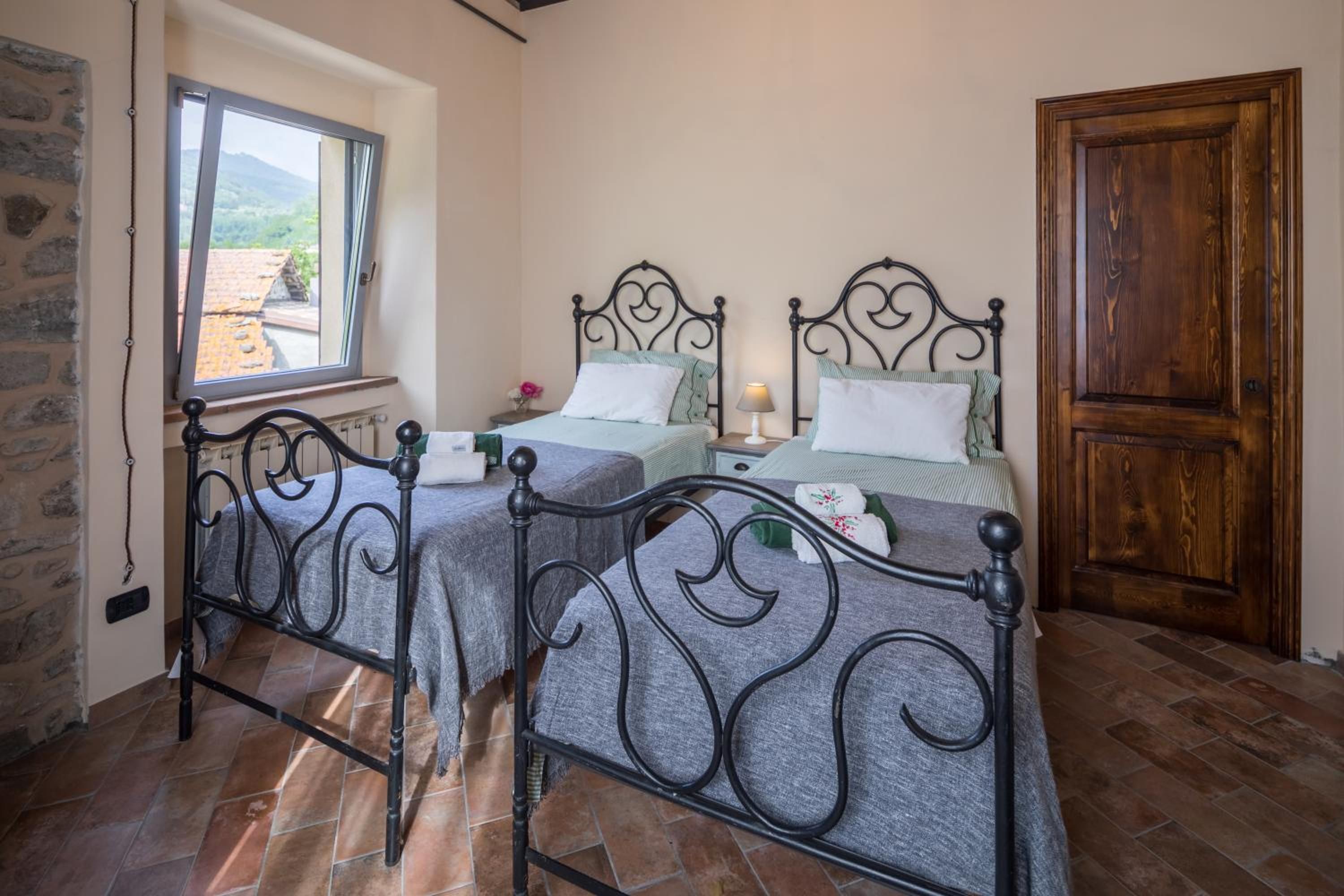 A room with two beds, a window, a stone wall, and a wooden door.