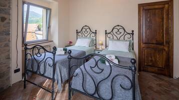 A room with two beds, a window, a stone wall, and a wooden door.