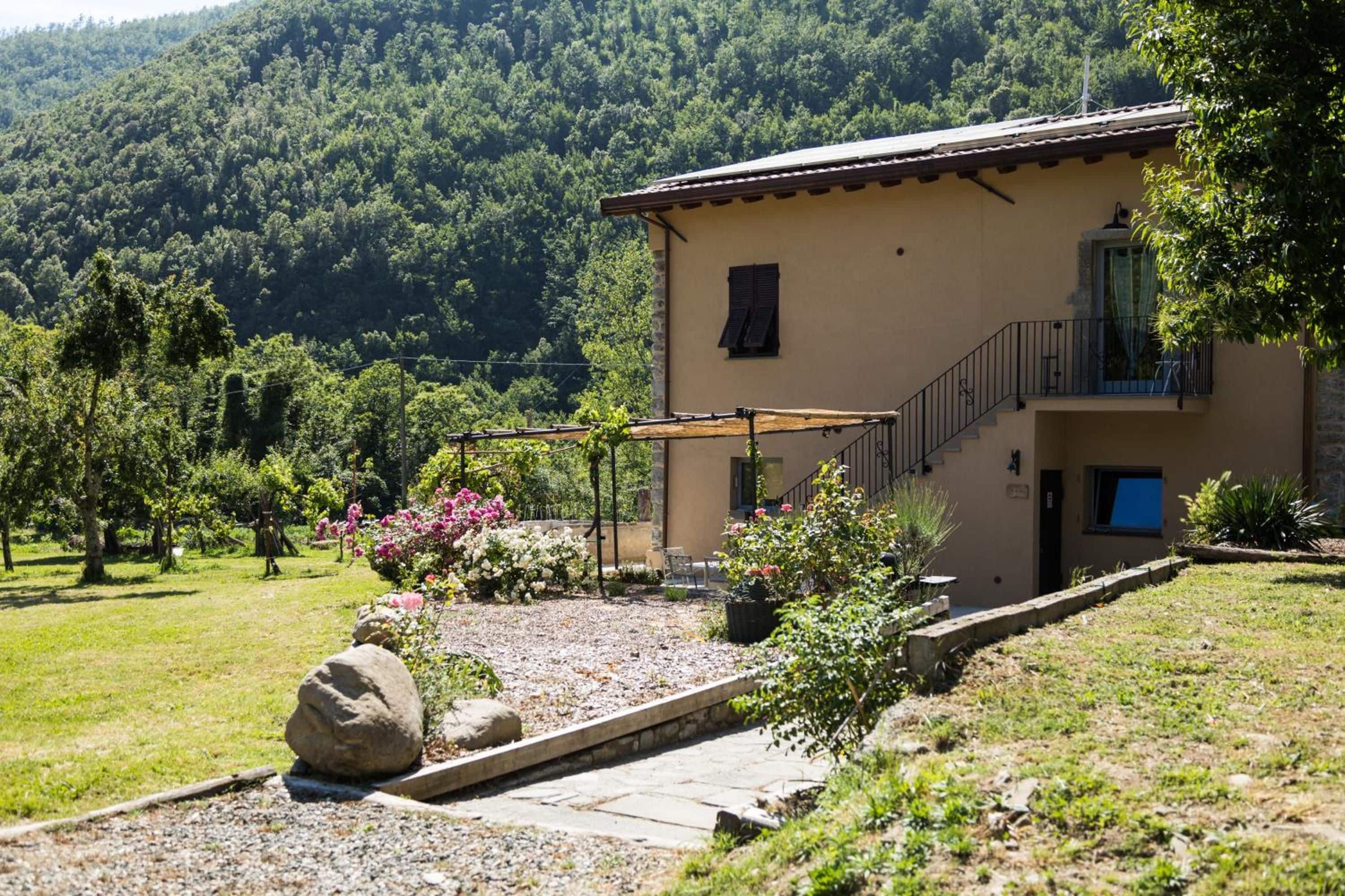 Ein zweigeschossiges Gebäude mit einer Steinfassade, einem Balkon und einem Garten mit blühenden Pflanzen und einem Weg.
