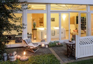 A modern outdoor patio with a lounge chair, a small table with candles, and a view of a spa area through glass doors. - Waldfrieden (Hitzacker)
