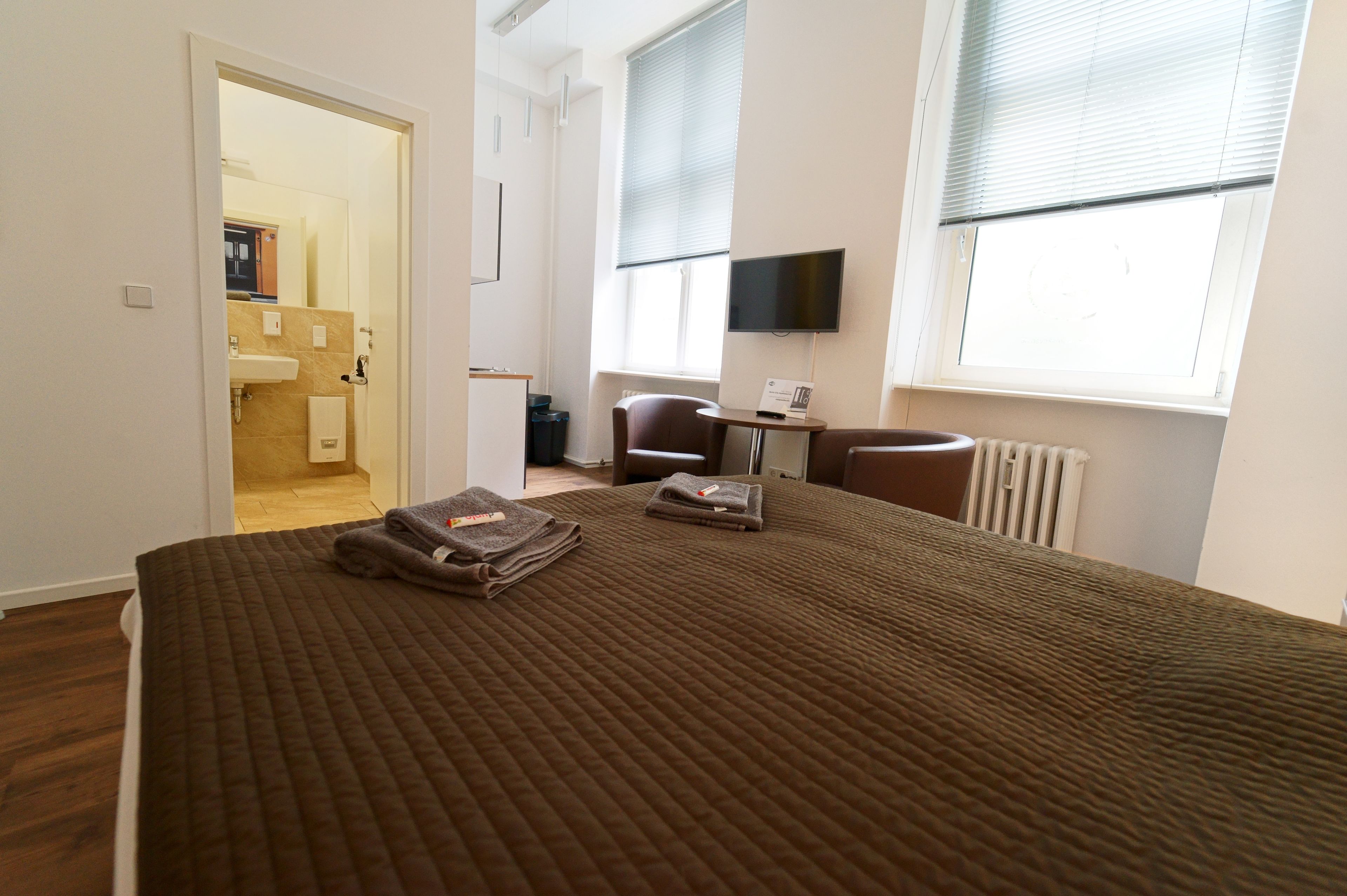 Una habitación de hotel con cama, escritorio, silla, televisor y ventana.