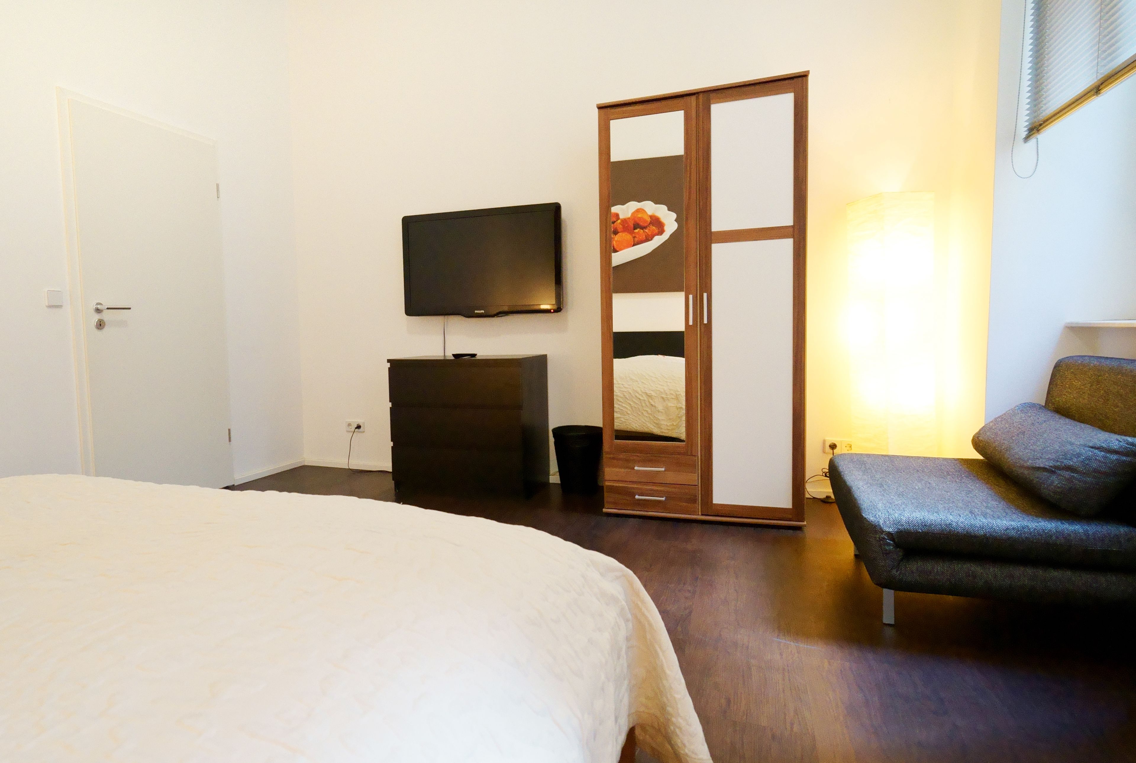 A bedroom with a bed, a wardrobe, a television, and a sofa.