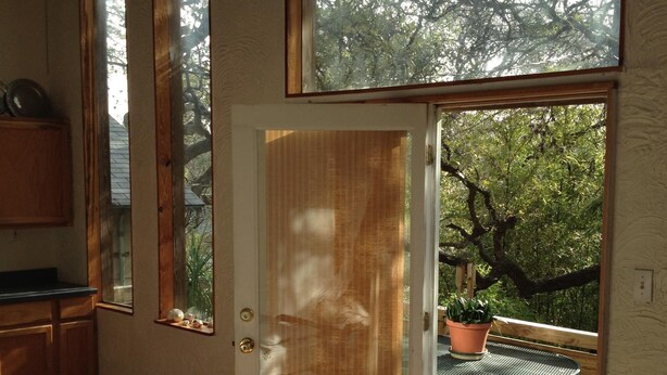 Una habitación con suelo de madera, una puerta corredera de cristal que da a un espacio exterior con una mesa y una planta en maceta.