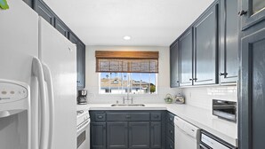 A kitchen with dark cabinets, a white refrigerator, a dishwasher, and a window with a view of buildings.