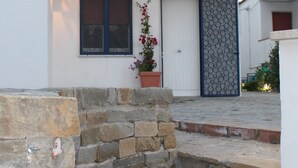 Ein modernes, zweistöckiges Gebäude mit weißer Fassade, einem kleinen Balkon, einem Blumentopf und einer Steintreppe, die zum Eingang führt.