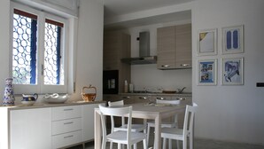 Eine moderne Küche mit weißen Schränken, einem Esstisch mit Stühlen und einem Fenster mit blauen Vorhängen.