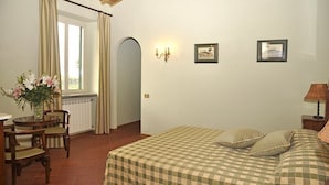 Une pièce comprenant un lit, un bureau et des chaises. Il y a une fenêtre avec des rideaux, un luminaire fixé au mur et un cadre photo.