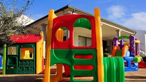 A colorful play structure with a red, green, and yellow design, located in front of a building with a red roof.