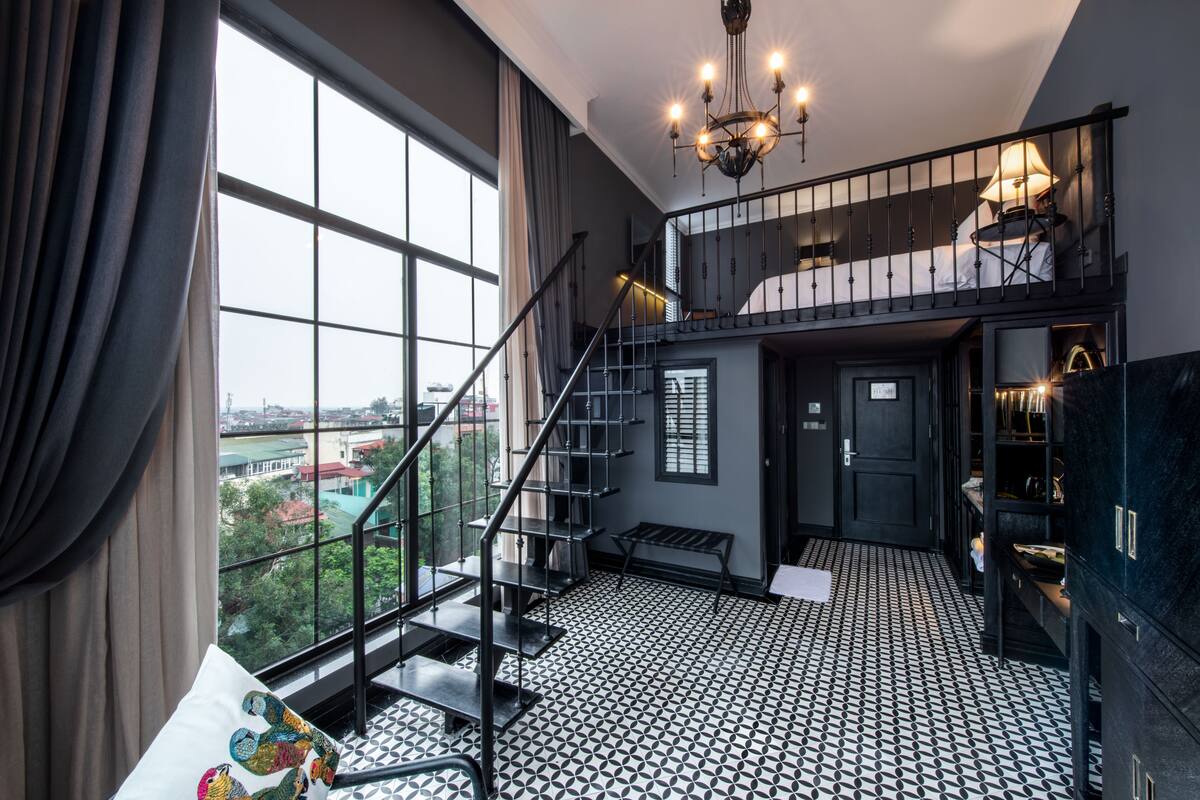 A spacious room with a large window, a staircase, and a chandelier.