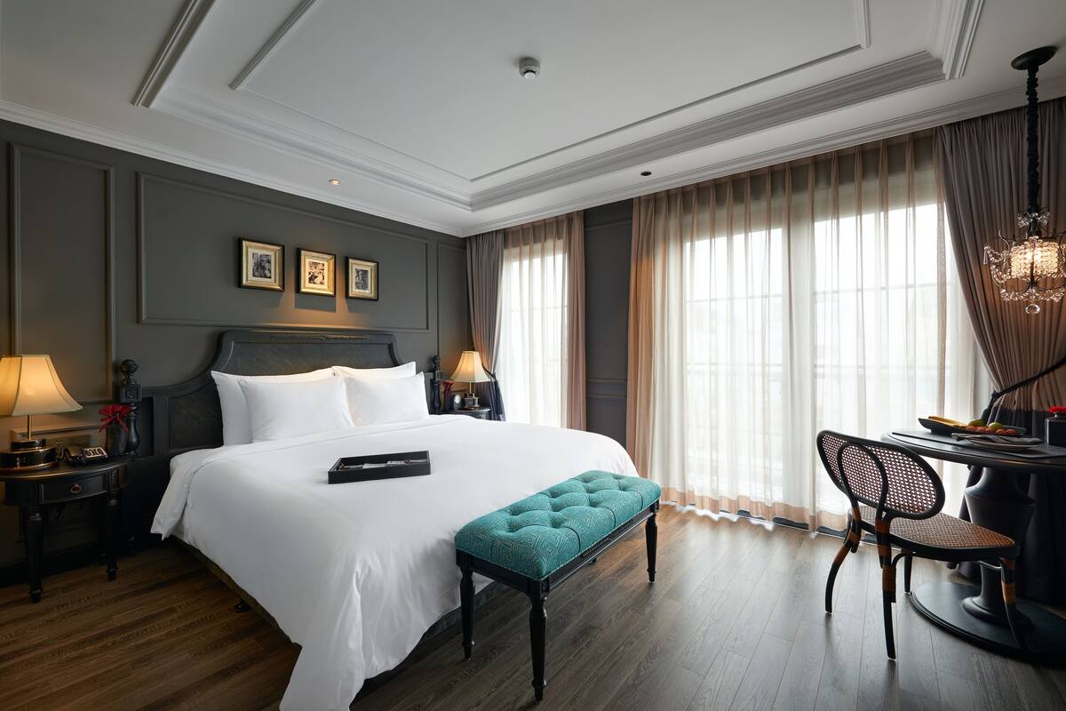A hotel room with a large bed, a bench, a desk, and a chair.