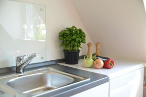 A kitchen with a stainless steel sink, a potted basil plant, and a white countertop. - Sonnenhaus Ferienwohnungen (Traben-Trarbach)