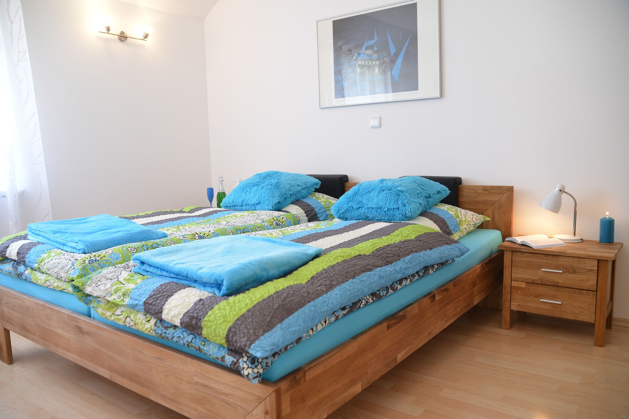 Una cama bien hecha con un edredón a rayas, una mesita de noche con una lámpara y un cuadro en la pared.