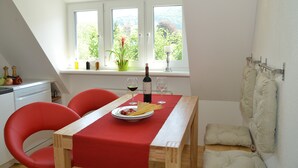 A dining area with a wooden table, red chairs, a red tablecloth, a plate of spaghetti, two wine glasses, and a bottle of wine. - Sonnenhaus Ferienwohnungen (Traben-Trarbach)