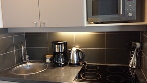 Una cocina con un lavamanos de acero inoxidable, una cafetera, un hervidor y un microondas.