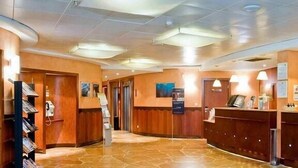 Un hall con mostrador de recepción, una escalera y un panel informativo en la pared.