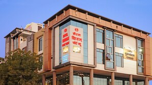 A modern hotel with a prominent sign in multiple languages, large windows, and a flat roof. - Hotel Shivam Fort View (Chittorgarh)