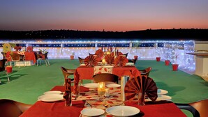 A dining area with tables set for two, featuring red tablecloths and leaf-patterned placemats. - Hotel Shivam Fort View (Chittorgarh)
