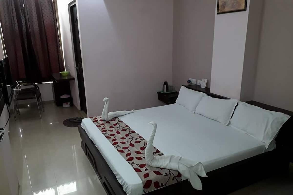 Ein Hotelzimmer mit einem ordentlich bezogenen Bett, einem kleinen Schreibtisch mit Stuhl und einem Nachttisch mit Lampe.