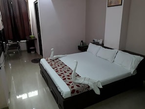 A hotel room with a neatly made bed, a small desk with a chair, and a nightstand with a lamp. - Hotel Shivam Fort View (Chittorgarh)