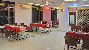 A dining area with tables set for four, air conditioning units, and a patterned curtain. - Hotel Shivam Fort View (Chittorgarh)
