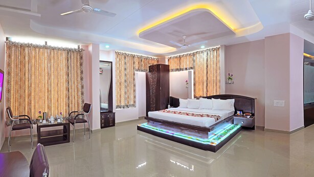 A modern hotel room with a large bed, a sofa, a TV, and a ceiling fan. - Hotel Shivam Fort View (Chittorgarh)