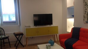 Un salon avec un téléviseur posé sur un meuble jaune, un canapé rouge, une petite table avec un plateau, et un fauteuil avec un coussin.