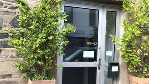 Une entrée en pierre, avec une porte en verre, deux plantes en pot et une boîte aux lettres.