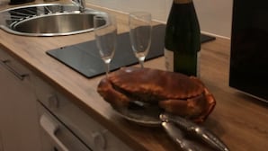 Un comptoir de cuisine avec un évier, une bouteille de champagne, deux verres à vin et une assiette avec un crabe.