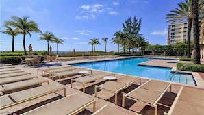 Un área de piscina con sillones de descanso y palmeras.