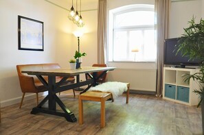 A dining area with a wooden table and chairs, a lamp, a radiator, a television, and a plant. - Gästehaus Schlossgarten (Langwedel)