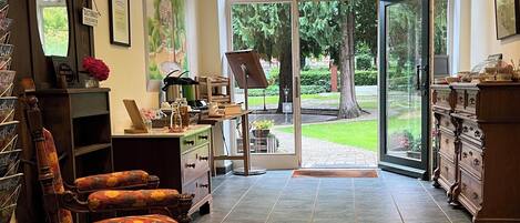A spacious room with a large arched glass door leading to a garden, a wooden chair with a floral cushion, and a wooden cabinet with drawers.