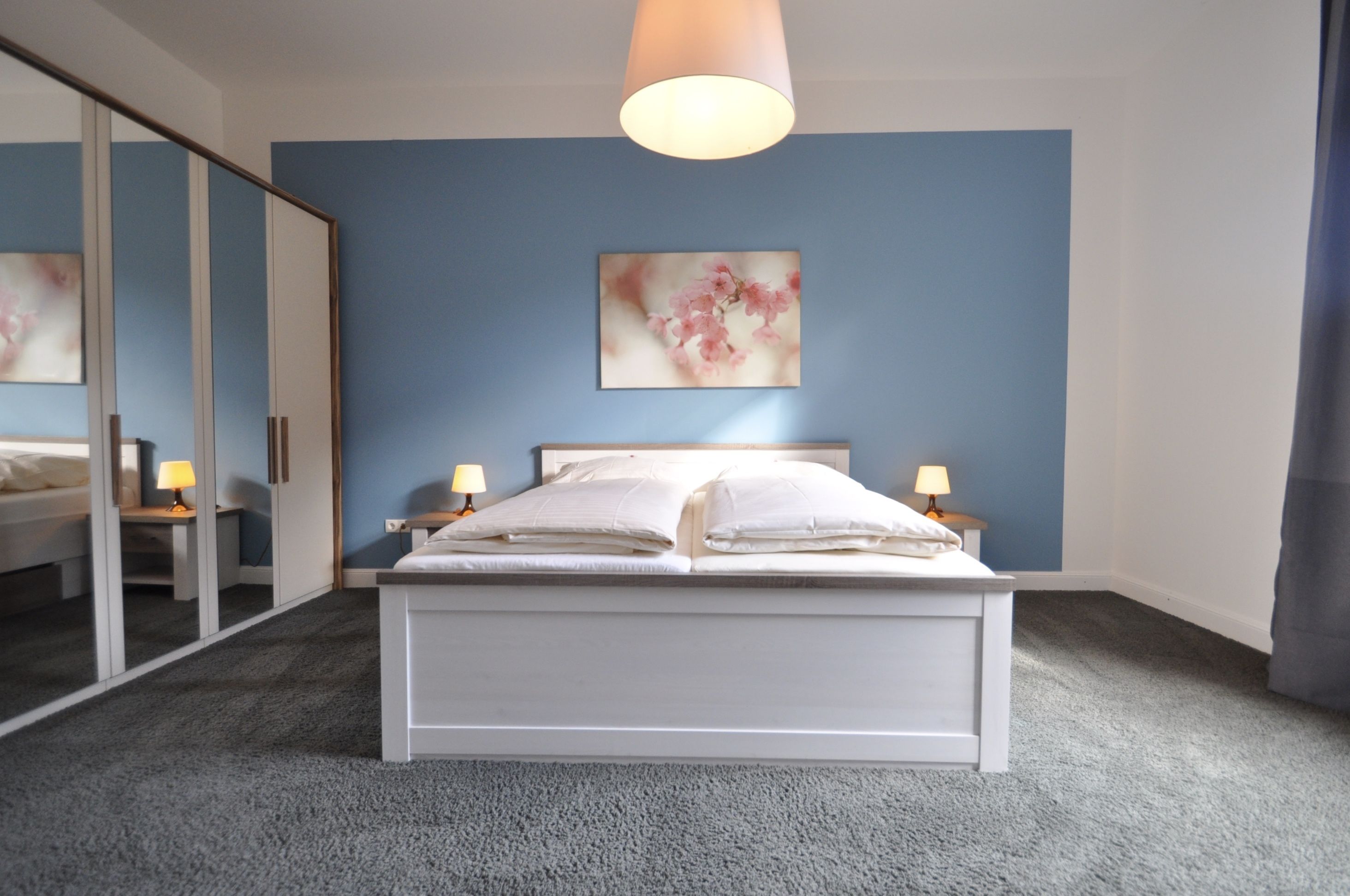Un dormitorio con cama, lámparas de noche, un espejo grande y una obra de arte en la pared.