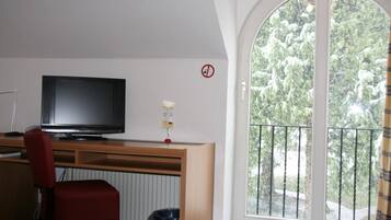 A room with a TV on a wooden desk, a red chair, a window with a view of trees, and a no smoking sign.