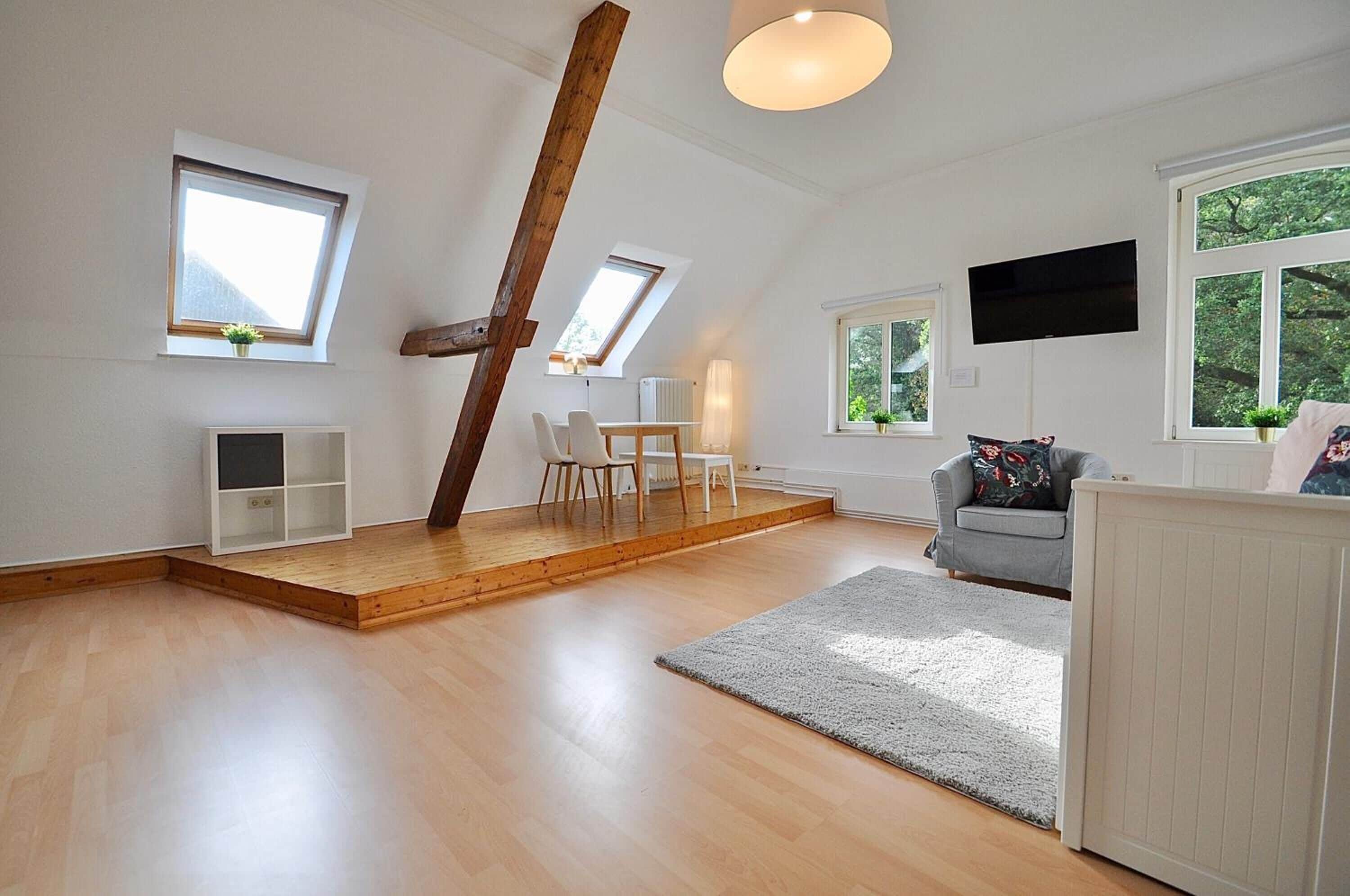 Geräumiges Schlafzimmer im Loft-Stil mit hohen Decken, Dachfenstern, einem Holzbalken, einem Bett, einem Schreibtisch und einem Fernseher.
