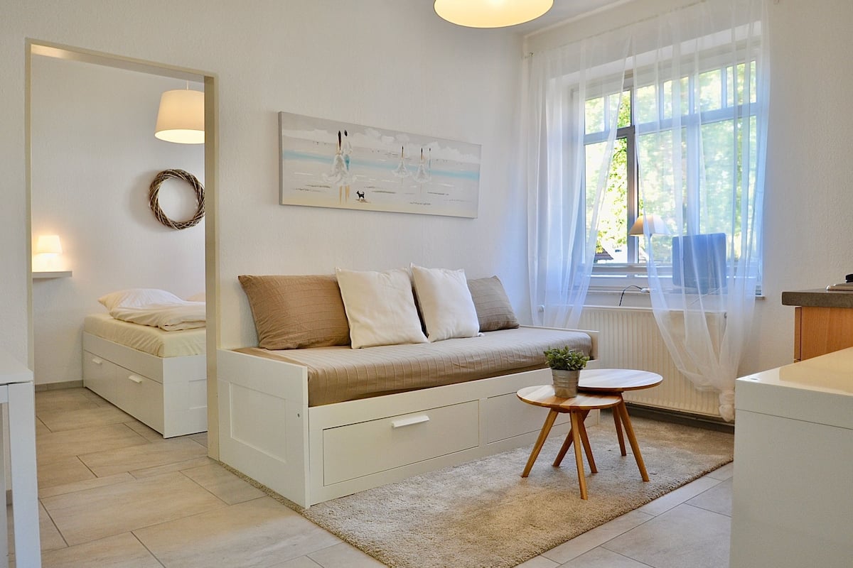 Una habitación moderna y luminosa con sofá cama, una mesita con una planta y un cuadro en la pared.