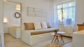 Una habitación moderna y luminosa con sofá cama, una mesita con una planta y un cuadro en la pared.