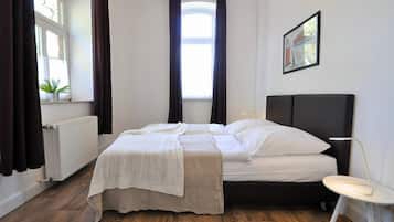 A bedroom with a bed, a radiator, a window with curtains, a chair, and a painting on the wall.