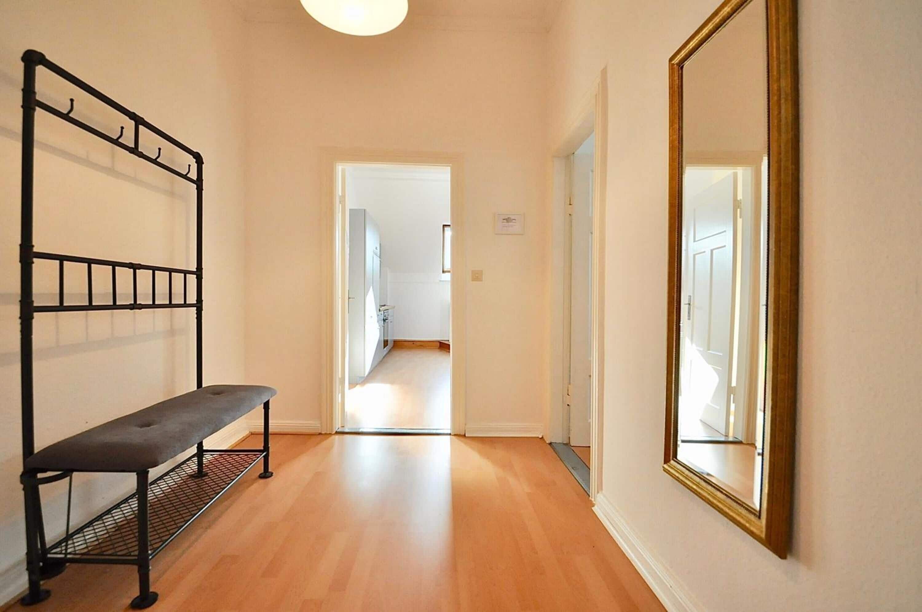 A hallway with a bench, a mirror, and a door leading to another room.