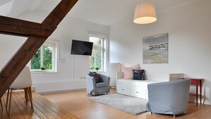 Ein modernes Wohnzimmer mit Holzboden, einem weißen Sofa, einem grauen Sessel und einem Fernseher an der Wand.
