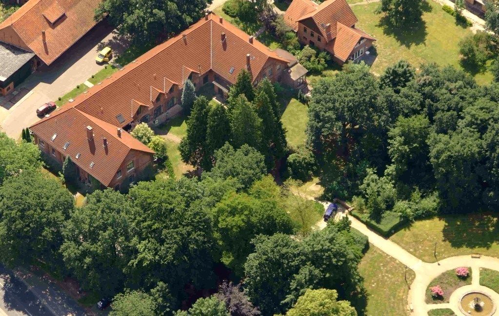 Vista aérea de um bairro residencial com várias casas de tijolo, rodeado por vegetação densa e um caminho circular central.