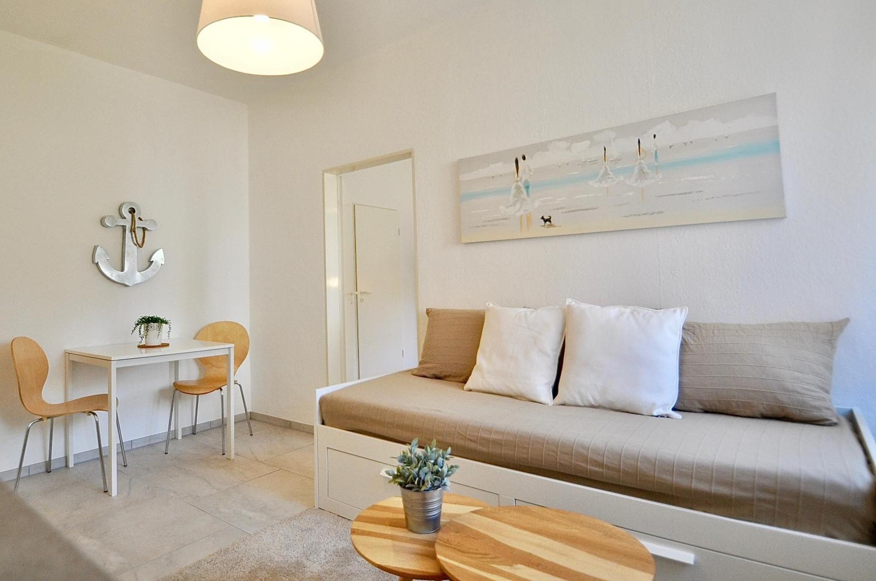 Une pièce minimaliste comprenant un lit, une petite table, deux chaises, un bureau et un tableau accroché au mur.