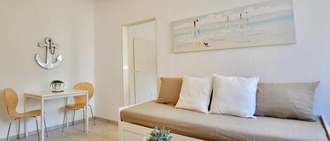 A minimalist room with a bed, a small table, two chairs, a desk, and a painting on the wall.