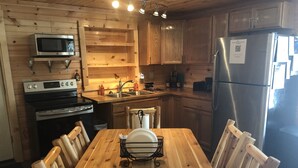 Een houten keuken met een eettafel, stoelen, een magnetron, fornuis, gootsteen en koelkast.