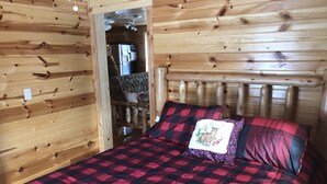Een houten kamer met een bed, een houten hoofdeinde en een zichtbare keuken met een koelkast.