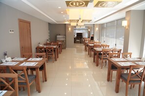 Uma área de refeições de hotel com mesas e cadeiras de madeira, um balcão de recepção e uma janela grande.