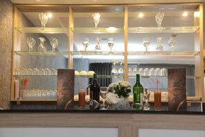 A bar area with multiple shelves of wine glasses and bottles, a menu stand, and a decorative vase with flowers. - Paris Prestige (Izmir)