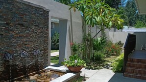 A modern outdoor patio with a stone wall, a water feature, and a variety of plants. - Residence Argine Apartments (Mahé Island)